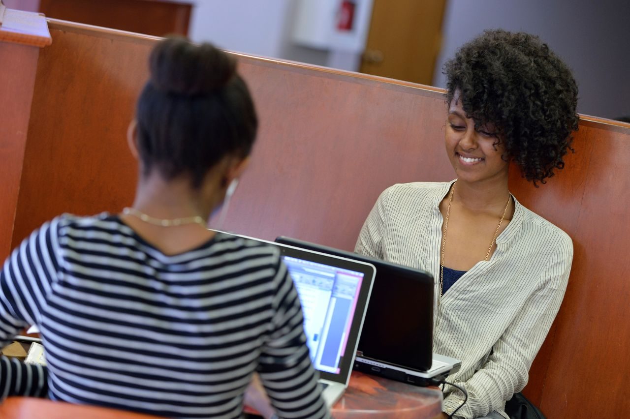 Two female students on their laptops in the cafe.