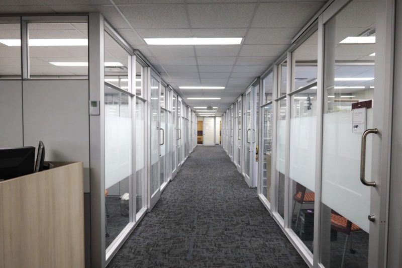 A carpeted hallway flanked by a dozen aluminum and glass rooms.