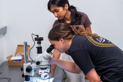 Varsha Durai, second from the left, helps Lauren Prillaman look at an object through the microscope in the Discovery Lab in the New  Undergraduate Science Laboratory Building on campus. Photo by Clark DeHart for Virginia Tech. 