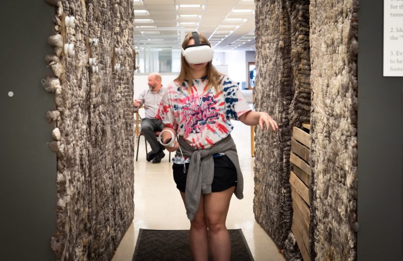 A female student walks through the exhibit wearing virtual reality gear.
