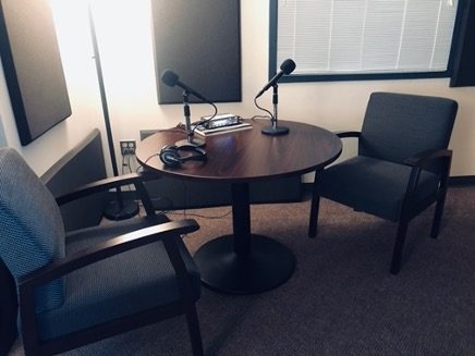 Two empty chairs at a small table with microphones in an interview booth.