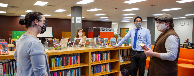 Faculty members stand around a short, long wooden shelf full of books.
