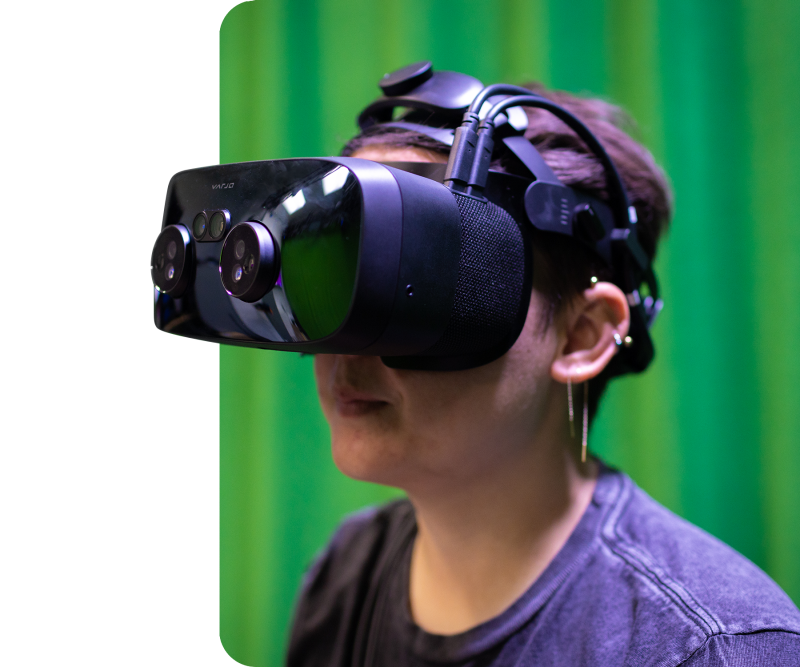 A student employee wearing a mixed reality headset that has multiple small lenses protruding from the faceplate.