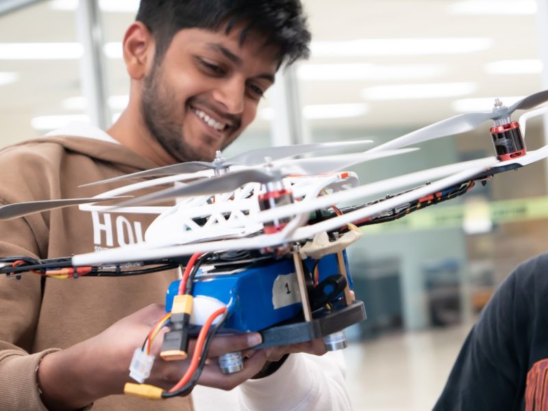  A student smiling as they hold a drone in their hand.