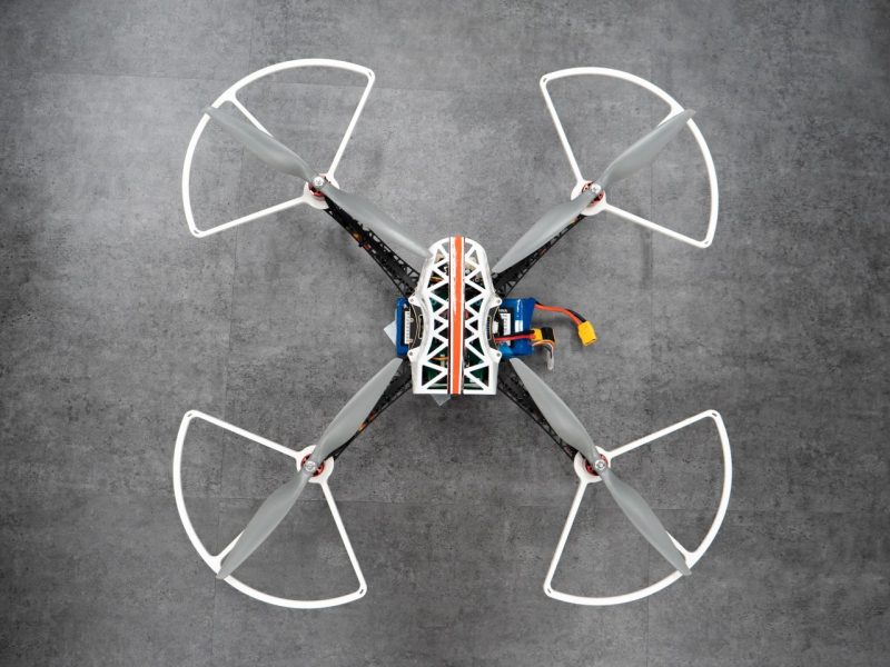 An unpowered drone sitting on the ground with two loose wires hanging to its side.