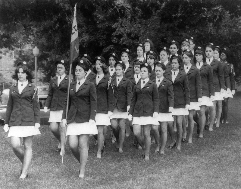 Two rows of women dressed in cadet uniforms marching across a field on the Virginia Tech campus.