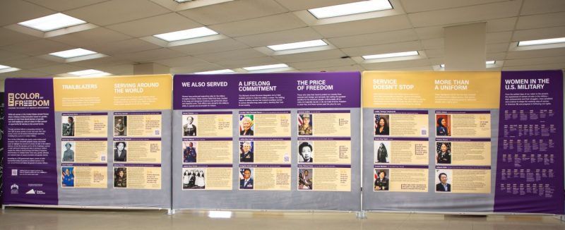 The Color of Freedom exhibit, consisting of three purple and gold walls displaying photos and descriptions of diverse military women.