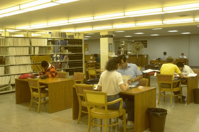 Several students work alone or in small groups at small wooden desks in an open space.